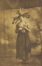 A performer in drag poses on stage wearing a head garment with sprawling feathers, [1910-1919?]. Creator: Unknown.
