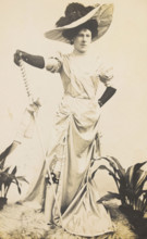 An man in drag is wearing a revealing dress and holding a staff, posing with his..., 1909. Creator: Unknown.