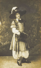 A man in drag wearing a very large hat with a veil, stands in front of a painted..., 1911. Creator: Unknown.