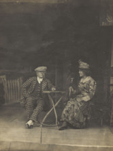 Two sailors, one in drag, sit on stage at a table, in front of very detailed scenery (1910-1919?). Creator: Unknown.