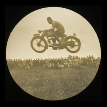 A view of a motorcycle jumping in front of a crowd of onlookers at an unknown..., 1920s-1930s.  Creator: Norman Kingsley Harrison.