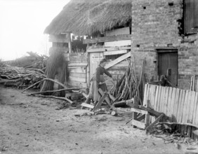 A woman sawing logs outside an outbuilding used as a wood store, Godstow, Oxford, Oxfordshire, 1900. Creator: Henry Taunt.