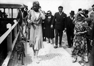 Vers 1930, à Deauville, le jour d'un Grand Prix, l'artiste Joséphine Baker se promène, tenant en
