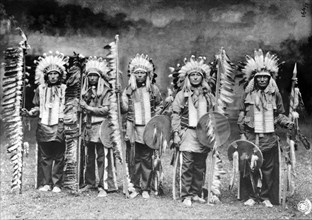 Carte photo représentant une tribu d'indiens debout, avec leurs armes