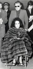 Elizabeth TAYLOR in a wheelchair with Richard BURTON, 1973