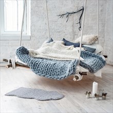 White loft interior in classic scandinavian style. Hanging bed suspended from the ceiling. Cozy large folded gray plaid, giant knit blanket, super chunky yarn, arm knitting. Trendy room design.