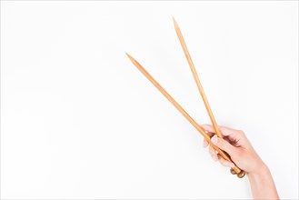 Woman hand with two wooden knitting needles over white background.