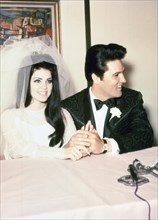 Elvis Presley and Priscilla Presley wedding photo, wearing tuxedo and wedding dress, smiling and holding hands, during a press conference following their marriage, May, 1967. Photo credit Smith Collec...