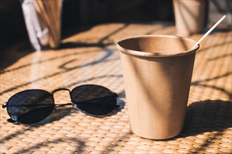 Disposable paper coffee cup on table in cafe with wooden stirrer,near sunglasses.Environmentally friendly lifestyle.Zero Waste,Save The Planet,Earth D