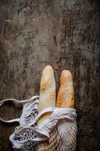 Fresh rosy baguettes in a string bag on a dark wooden retro background. Top view, copy space