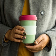 Bamboo eco cup in the hands of a woman in a gray coat and a yellow autumn sweater