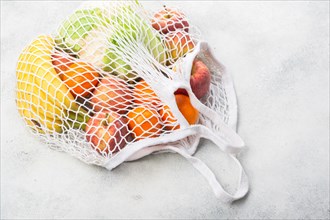 Zero waste eco friendly shopping concept, vegetables fruits in white mesh bag on white kitchen table, selective focus