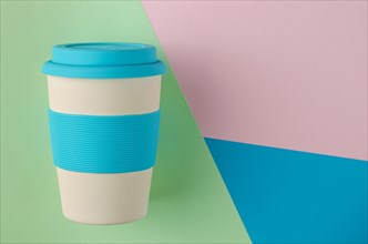Reusable bamboo coffee cup with silicone holder and lid on colorful background. Flat lay, copy space.