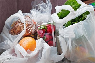 Plastic shopping bags are filled with grocery store purchases.