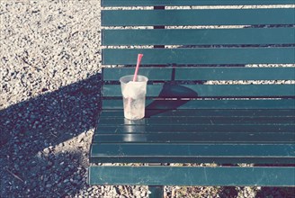 disposable plastic drinks cup with straw lying on bench.