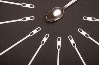 White stirring sticks lying around metal teaspoon on black background. Fast food against homemade food.