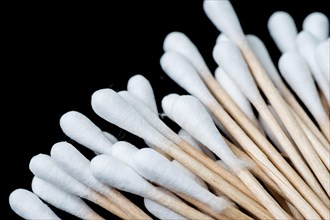Pile of cotton swabs, q tips, spread out like a fan. The swabs are photographed against a black background