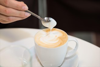 female hand holding a spoon over a hot cup of coffee Cappuccino