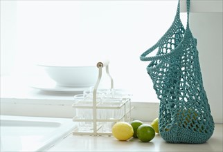 Crocheted string bag on kitchen worktop with lemons and limes