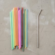 One reusable metal straw against the heap of plastic disposable drinking straws. Zero waste concept