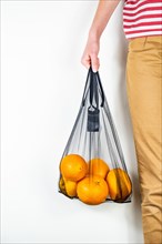 Holding a reusable string bag full of oranges. Sustainable eco packaging concept: shopping for groceries with a multi-use bag to reduce ecological foo