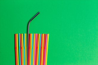 Stainless steel reusable drinking straw with plastic straws on green background