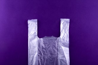 White torn plastic shopping, grocery bag on purple background. Pollution concept.