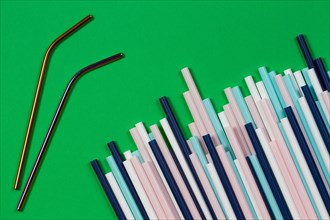 Two stainless steel reusable drinking straws with many multicolored plastic straws on green background