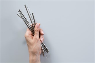 Metallic reusable straws and brush in female hand on grey background. Sustainable lifestyle concept. Zero waste, plastic free. Pollution environment.