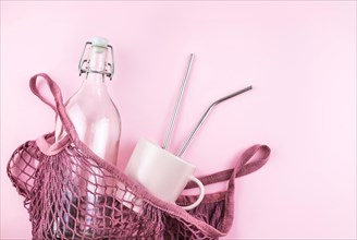 Mesh bag with reusable glass water bottle and cup on pink background. Sustainable lifestyle. Zero waste and no plastic concept.