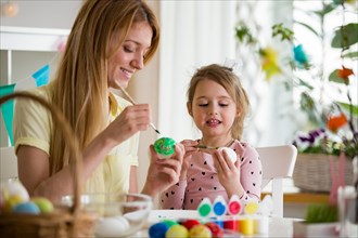 A mother and daughter celebrating Easter, painting eggs with brush. Cute little girl in bunny ears preparing the holiday.