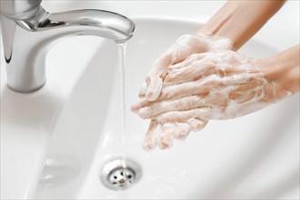 Hand Washing in white sink. Water flows from a faucet at soapy female hands. Covid-19 coronavirus protective measure.