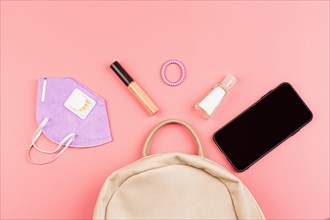 Flat lay of leather woman bag open out with face mask, sanitizer hand gel to protect from Coronavirus or COVID-19, lipstick, accessories and