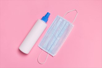 Coronavirus protection. Medical surgical mask and disinfectant or hand sanitizer on pink background. Hygiene measures to prevent spread of Covid-19 pa