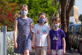 Three young sisters aged five years, 8 years & 10 years wearing masks that they've made at home with mum to wear during the COVID-19 / COVID 19 coronavirus pandemic of 2020; homemade face mask. UK. (1...