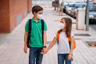 Boy and girl with backpacks and masks go to school in the coronavirus pandemic
