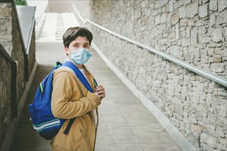 portrait of a kid with medical mask and backpack waiting at the school door outdoor