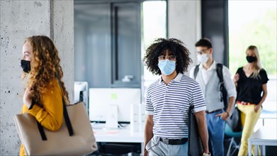 Young people with face masks back at work in office after lockdown, walking.