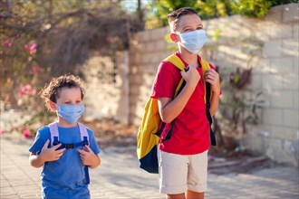 Pupils with medical masks on face and backpacks outdoor. Education during coronavirus time. Children and healthcare. Back to school.
