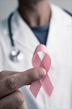 closeup of a young caucasian doctor man with a pink ribbon for the breast cancer in his hand