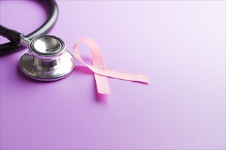 Pink breast cancer ribbon. Breast cancer symbol and stethoscope on violet background.