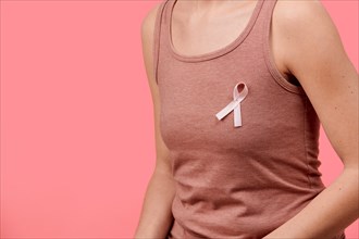 Midsection of a young woman wearing pink breast cancer awareness ribbon isolated over living coral background. Healthcare, people, charity and medicin