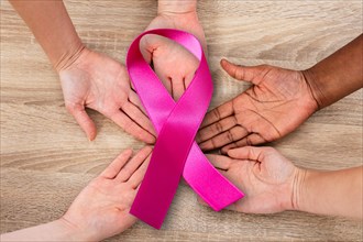 Elevated View Of Hand Joined In Circle Holding Breast Cancer Symbol Against Wooden Background