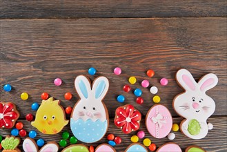 Crop of colorful ginger glazed cookies and chocolate balls isolated on wooden background. Close up of homemade lovely delicious pastry in shape of easter animals, eggs and red flowers.