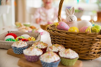 Easter celebration, close-up table with glazed cupcakes, basket with Easter eggs and bunny. Happy family holiday.
