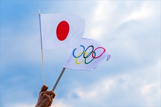 Fan waving the national flag of Japan and the Olympic flag with symbol olympics rings.