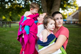 Lesbian mothers holding wet children wrapped in a towel in summer yard
