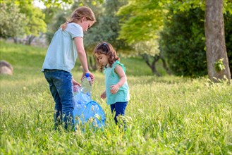 Cute little girls cleaning up plastic litter on grass. Children Volunteers cleaning up litter and putting plastic bottle into recycling bag. World Environment Day.