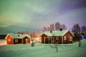 Northern Lights (aurora borealis) over traditional scandanavian houses in Akaslompolo village, a small town in Finnish Lapland, inside Arctic Circle in Finland