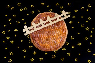 Galette des rois, french kingcake with a golden crown on a black slate background with golden star-studded